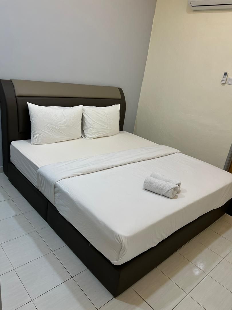 A bed with a headboard, white bedding, and a rolled towel on the footboard.