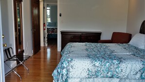 Ein Schlafzimmer mit einem Bett, einem Deckenventilator, Holzboden und einer Tür zu einem anderen Raum.