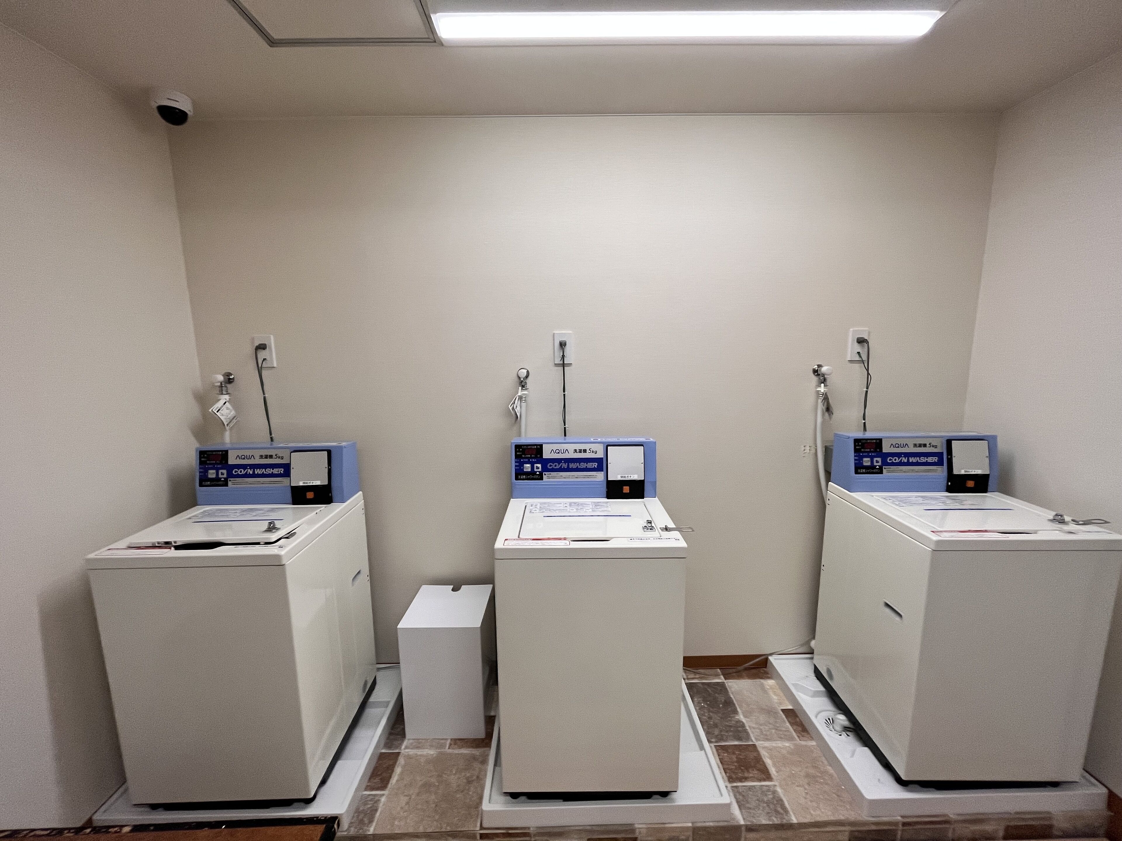 A laundry facility with three washing machines, each equipped with a control panel and a water inlet.