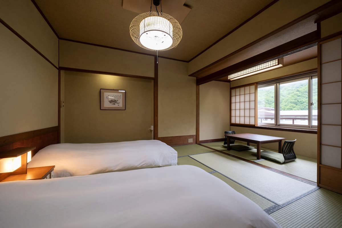 A traditional Japanese room with tatami flooring, a low table, two beds, and a hanging light fixture.