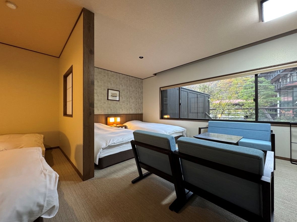 A hotel room with two single beds, a small table, and a view of the outside.