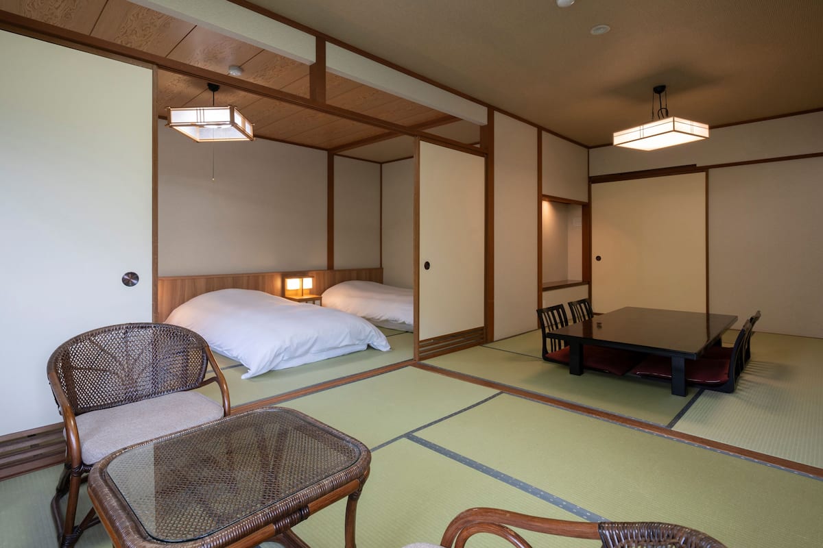 A traditional Japanese room with tatami flooring, a low table, and a bed with white bedding.