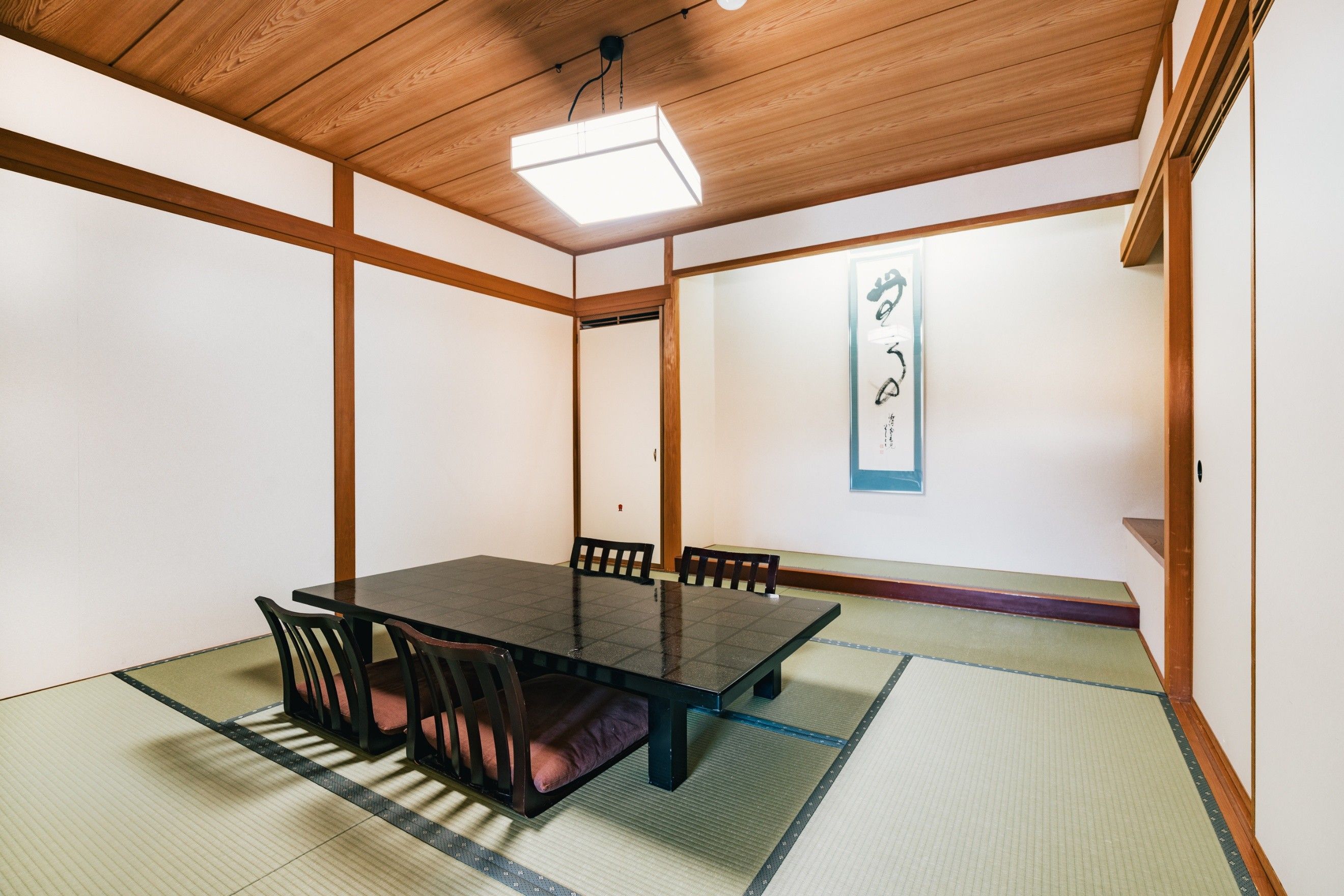 A traditional Japanese-style room with tatami flooring, a low wooden table, and black chairs.