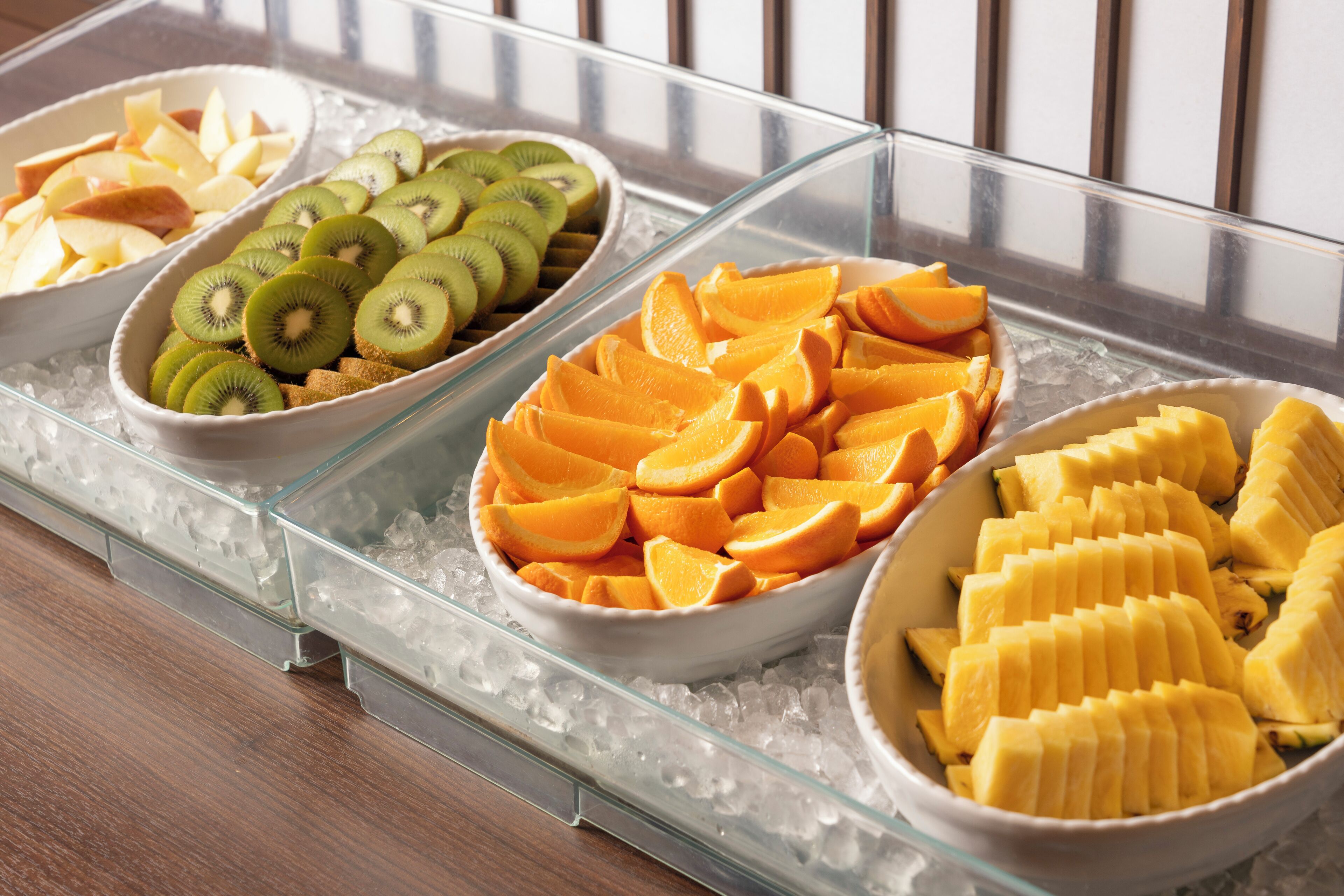 Een buffet met schalen vol gesneden fruit op een glazen schaal boven ijs.