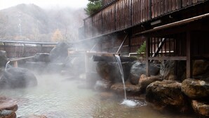 Une structure traditionnelle en bois, agrémentée d’une fontaine en pierre et d’un pont en bois.