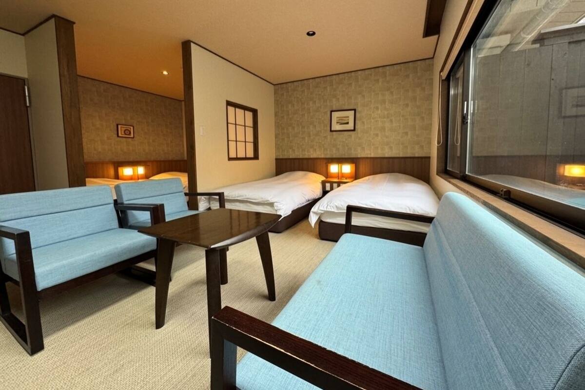 A hotel room with a sofa, a small table, two single beds, and a window with a view.