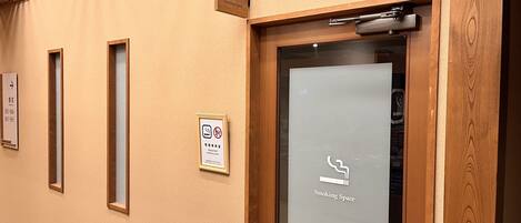 Un pasillo con un letrero de área para fumadores, una puerta con el símbolo de fumar y un cartel que indica una sala de fumadores designada.