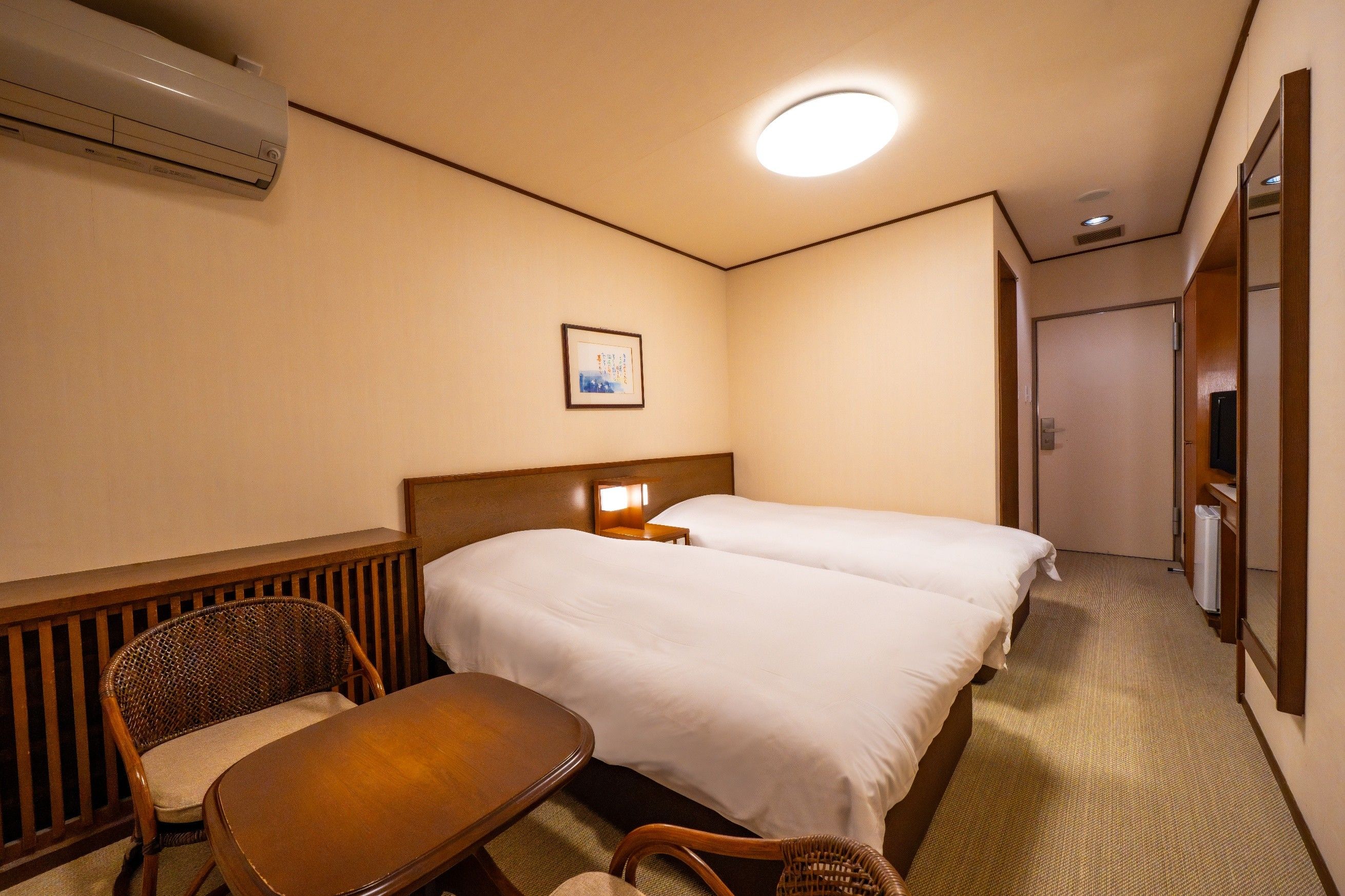 Habitación de hotel con dos camas, una silla, una mesa y un cuadro en la pared.