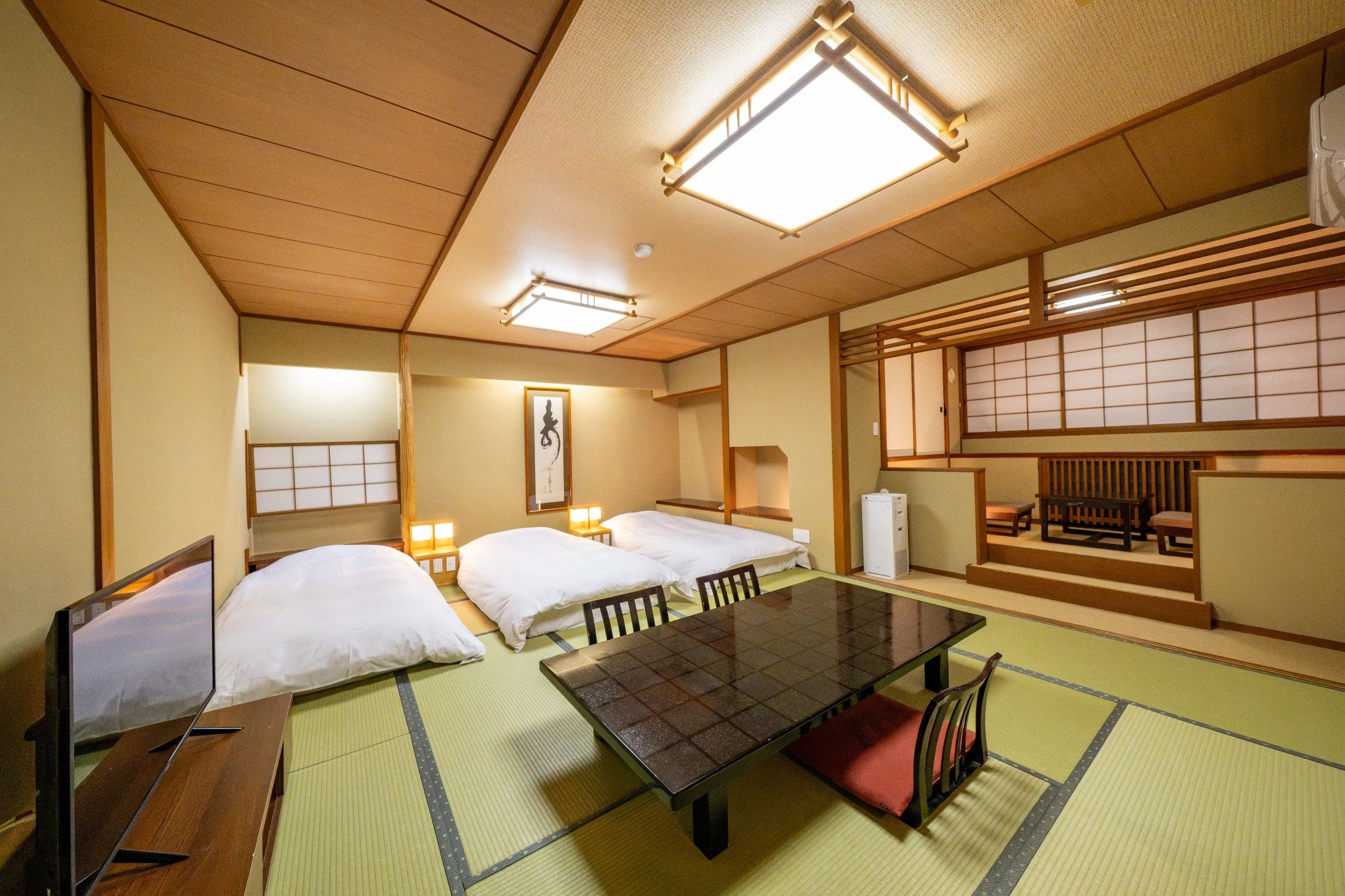 Una habitación de estilo japonés tradicional, con suelo de tatami, dos camas, una mesa baja y puertas correderas.