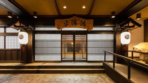 Une entrée de style japonais traditionnel, avec un sol en pierre, des poutres en bois et une enseigne au-dessus des portes.