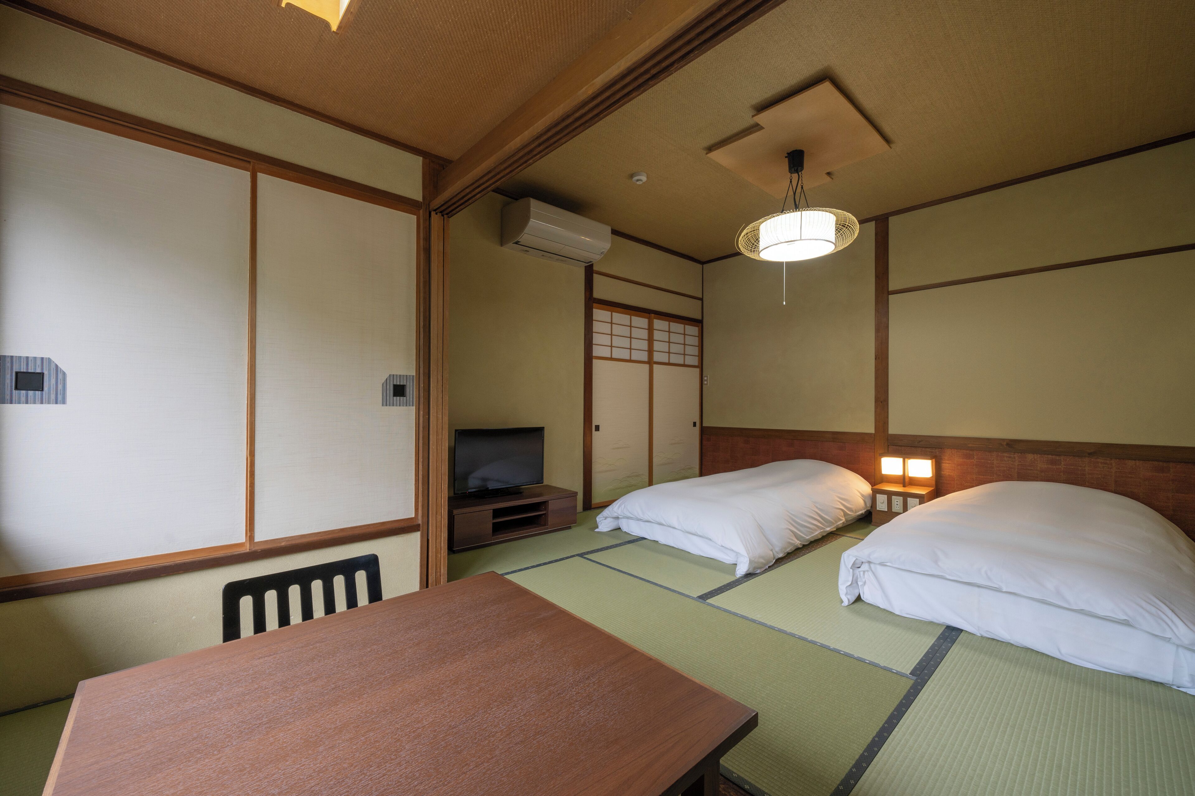 Une pièce de style japonais traditionnel, avec un sol recouvert de tatamis, une table en bois, un téléviseur et un futon servant de lit.