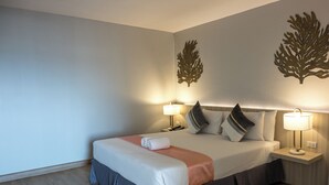 Ein ordentlich bezogenes Bett mit grau-weißer Tagesdecke, zwei Nachttischlampen und dekorativen Wandbildern.