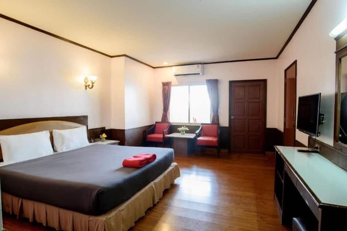 Ein Hotelzimmer mit einem großen Bett, einem Schreibtisch, einem Sessel, einem Fernseher und einem Fenster mit Vorhängen.