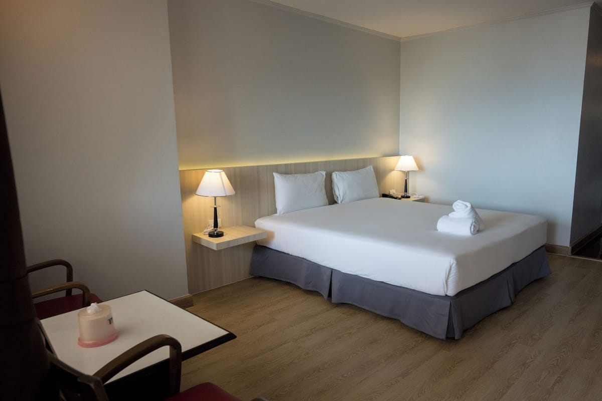 Ein Hotelzimmer mit einem ordentlich bezogenen Bett, zwei Nachttischen mit Lampen, einem kleinen Tisch mit Taschentuchbox und einem Stuhl.
