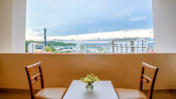 Ein Zimmer mit großem Fenster und Blick auf eine Stadtlandschaft, einem Tisch mit zwei Stühlen und einer Vase mit Blumen.