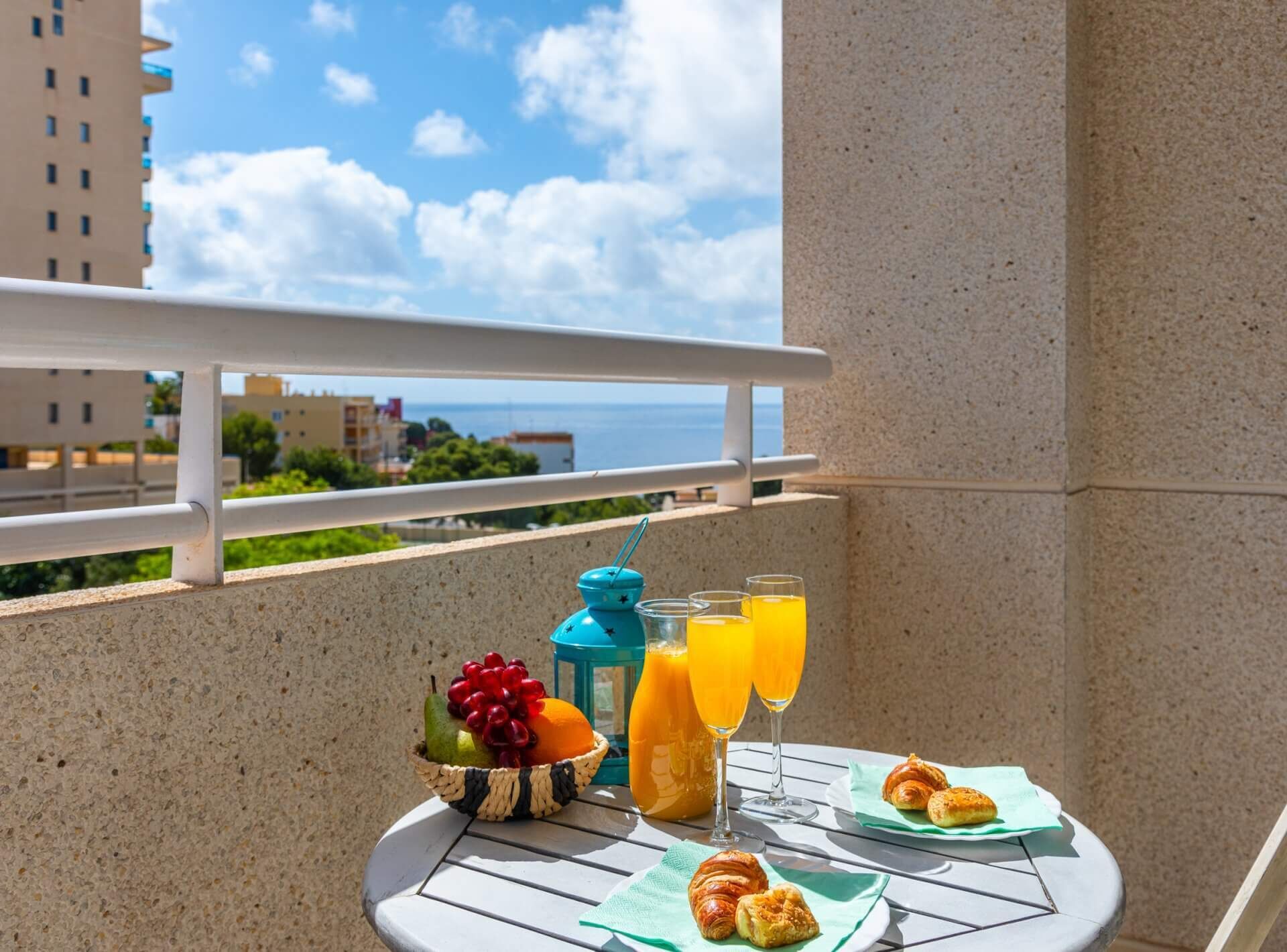 Uma varanda com mesa posta para o café da manhã, incluindo croissants, uma saladeira de frutas e copos de suco de laranja.