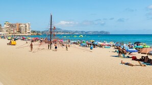 Ein Strand mit Liebespaaren, Volleyballspielern, Sonnenschirmen und einem strahlend blauen Himmel.