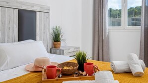 Ein Hotelzimmer mit einem Bett, einem Tablett mit Handtüchern, einer roten Tasse, einem Hut und einer kleinen Pflanze.