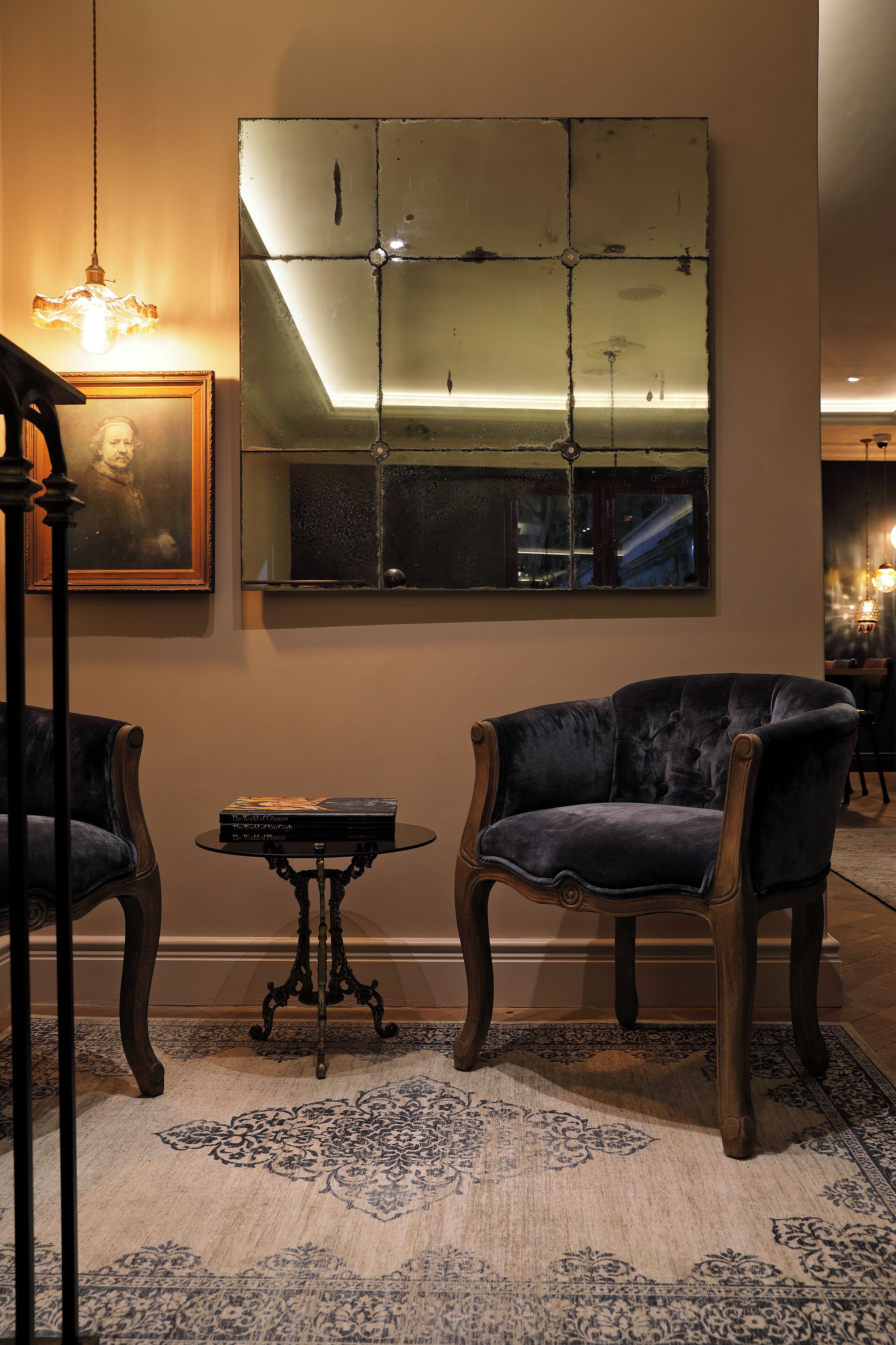 A room with two dark armchairs, a small table, a framed picture, and a large mirror on the wall.