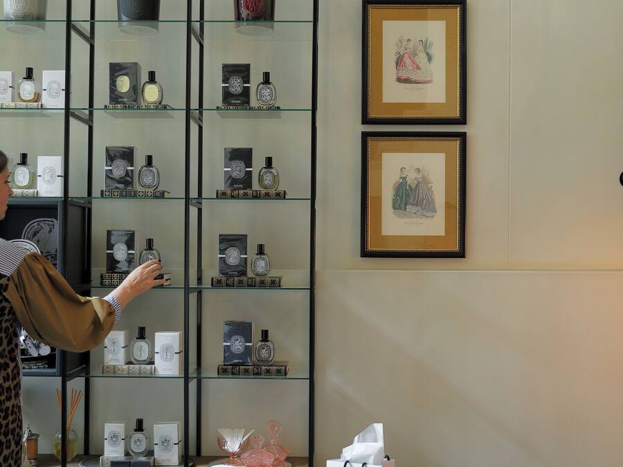 A person browsing a glass display of perfume bottles in a boutique setting.