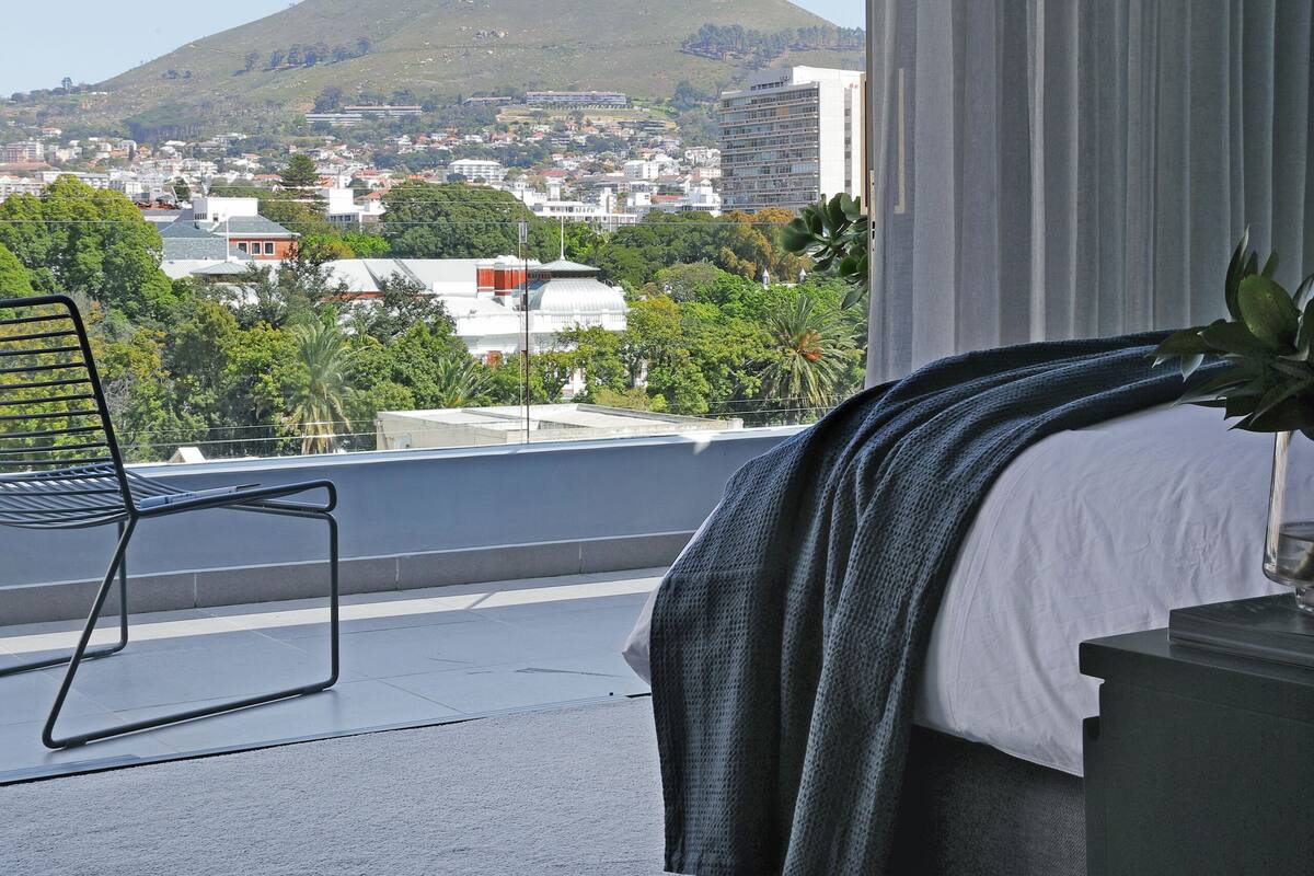 A hotel room with a bed, a chair, a view of a mountain, and a cityscape.
