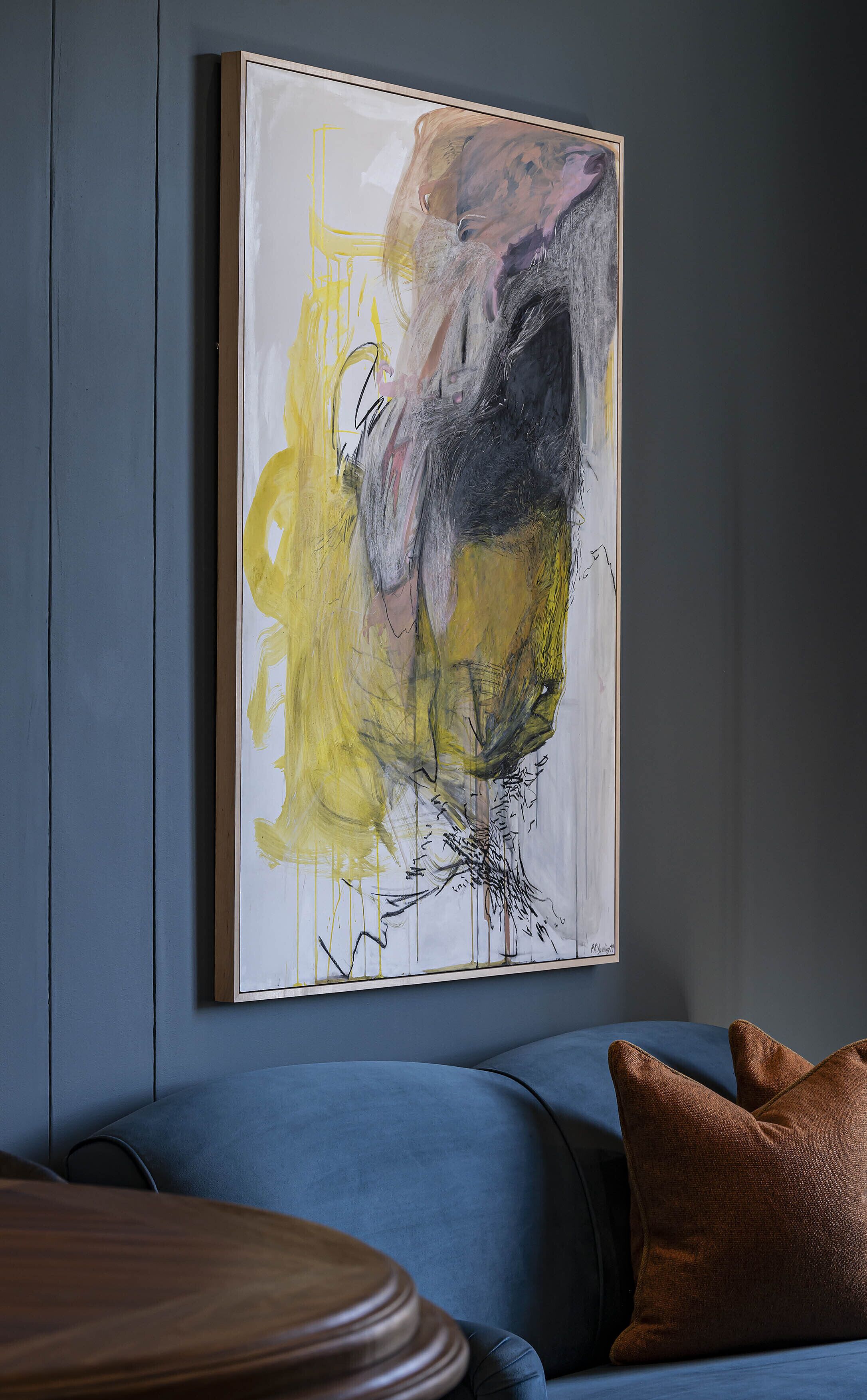 Um quarto com uma pintura abstrata grande na parede, um sofá azul e uma mesa de madeira.