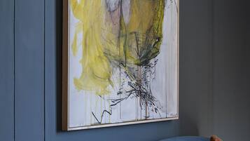 Um quarto com uma pintura abstrata grande na parede, um sofá azul e uma mesa de madeira.