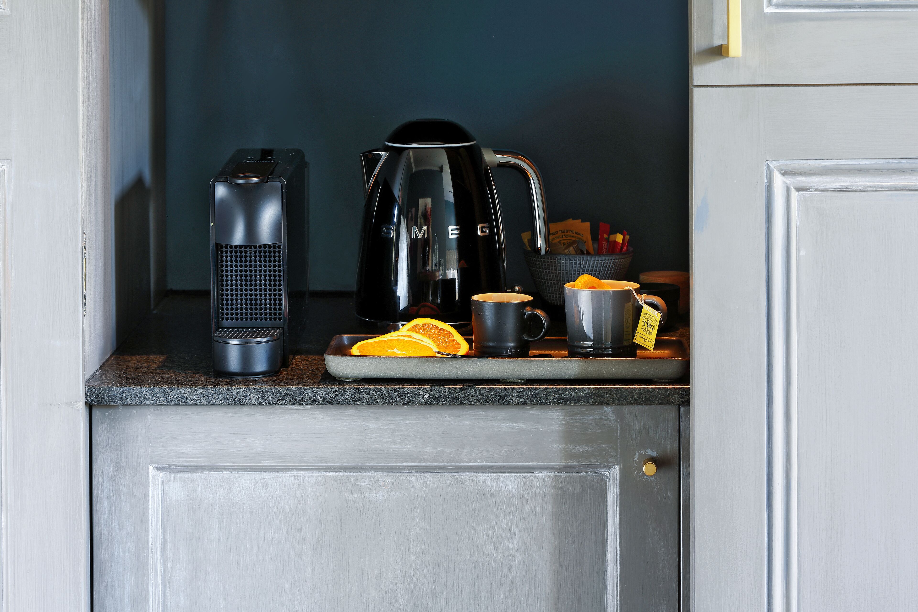 Eine Küchenarbeitsplatte mit einer Kaffeemaschine, einem Wasserkocher und einer Schale mit Orangenscheiben.