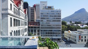A modern building with a glass facade, a pool area, and a view of a mountain. - Labotessa Luxury Boutique Hotel (Cape Town)