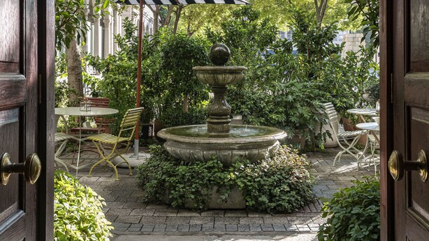 A courtyard with a stone fountain, outdoor seating, and a view of trees and buildings. - Labotessa Luxury Boutique Hotel (Cape Town)