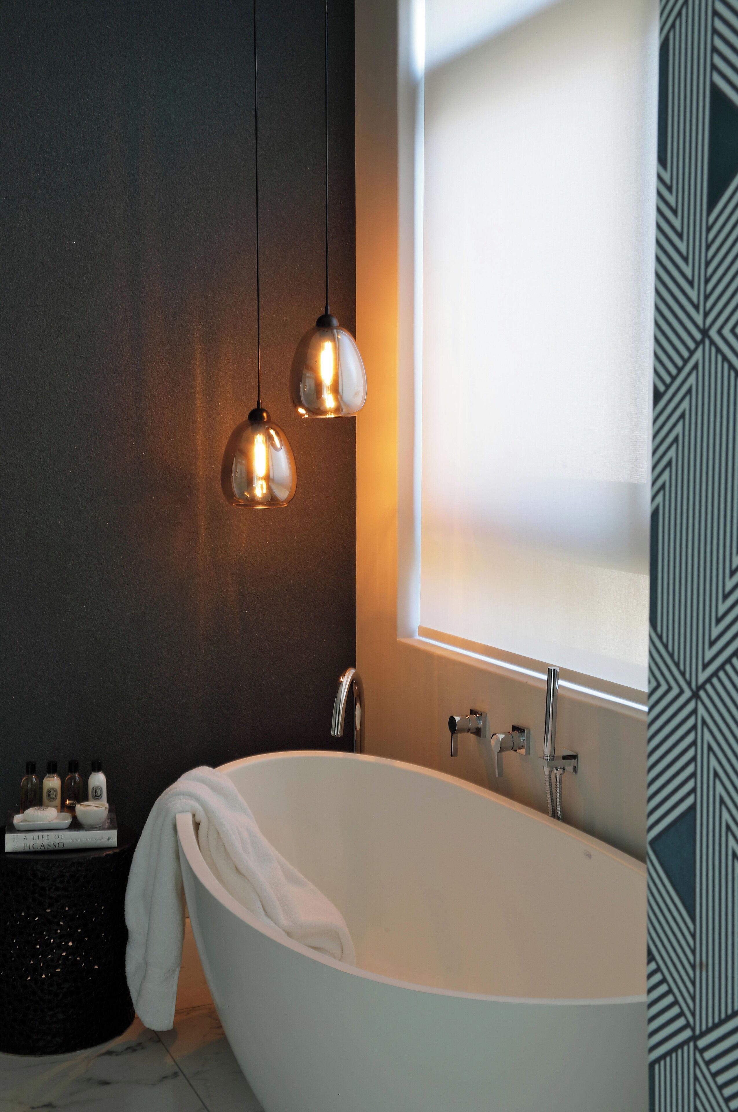 A modern bathroom with a freestanding bathtub, pendant lighting, and a window with frosted glass.