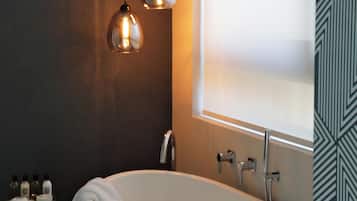 A modern bathroom with a freestanding bathtub, pendant lighting, and a window with frosted glass.