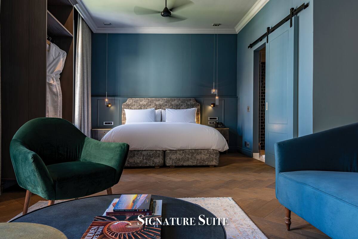 A bedroom with a large bed, a green armchair, a blue sofa, and a small table with books.