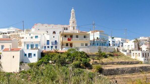 A coastal village with white buildings, a prominent church with a bell tower, and a clear blue sky.