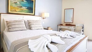 A hotel room with a bed, a bedside table with a lamp, a desk with a chair, a painting on the wall, and a mirror.