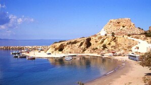 A coastal area with boats docked near a sandy beach, rocky cliffs, and a small building.
