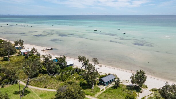 A beach with clear turquoise waters, a sandy shore, and several small buildings with roofs. - Pet Friendly - Cutest Cottage on Fourth walk to the Beach (Rosebud)