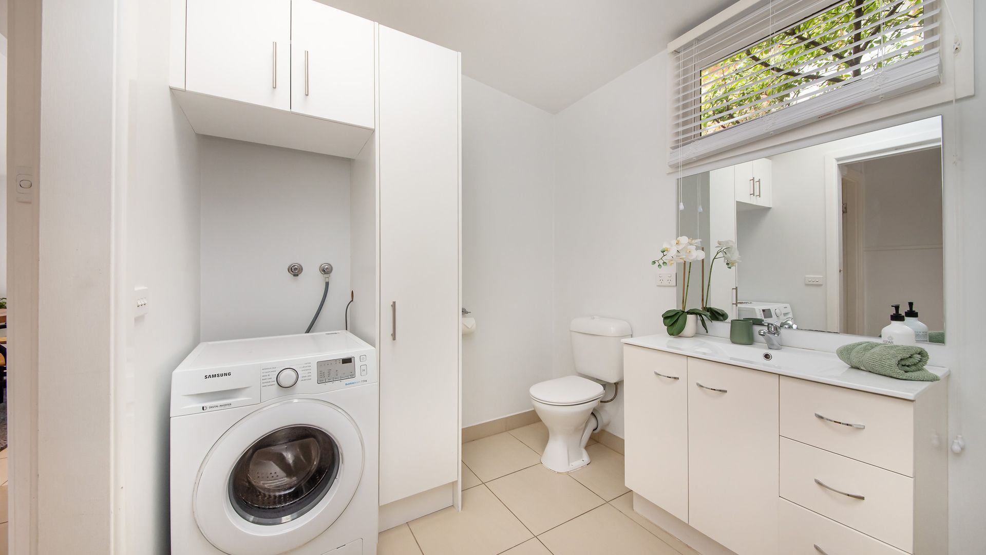 A modern bathroom with a washing machine, toilet, and vanity with a mirror.