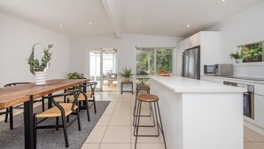A modern kitchen with a wooden dining table, bar stools, and a white countertop. - Pet Friendly - Cutest Cottage on Fourth walk to the Beach (Rosebud)