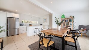 A modern kitchen with a central island, a dining area with a wooden table and chairs, and a cozy seating area with a sofa and a bookshelf. - Pet Friendly - Cutest Cottage on Fourth walk to the Beach (Rosebud)