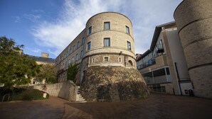 A historic building with a round tower, a stone wall, and a modern extension.