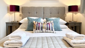 A neatly made bed with a grey headboard, two bedside tables with lamps, and a colorful abstract painting on the wall.