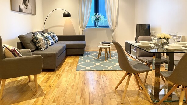 A modern living room with a sofa, chairs, a dining table set for four, and a large window with curtains.