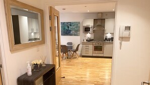 A modern kitchen with stainless steel appliances, a dining area with a table and chairs, and a wooden floor.