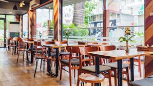 A restaurant interior with wooden tables and chairs, large windows, and a view of the street outside.