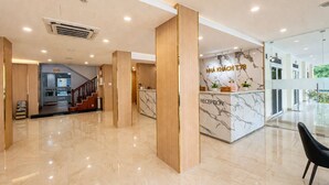 A modern hotel lobby with a reception desk, marble flooring, and a staircase leading to another area.