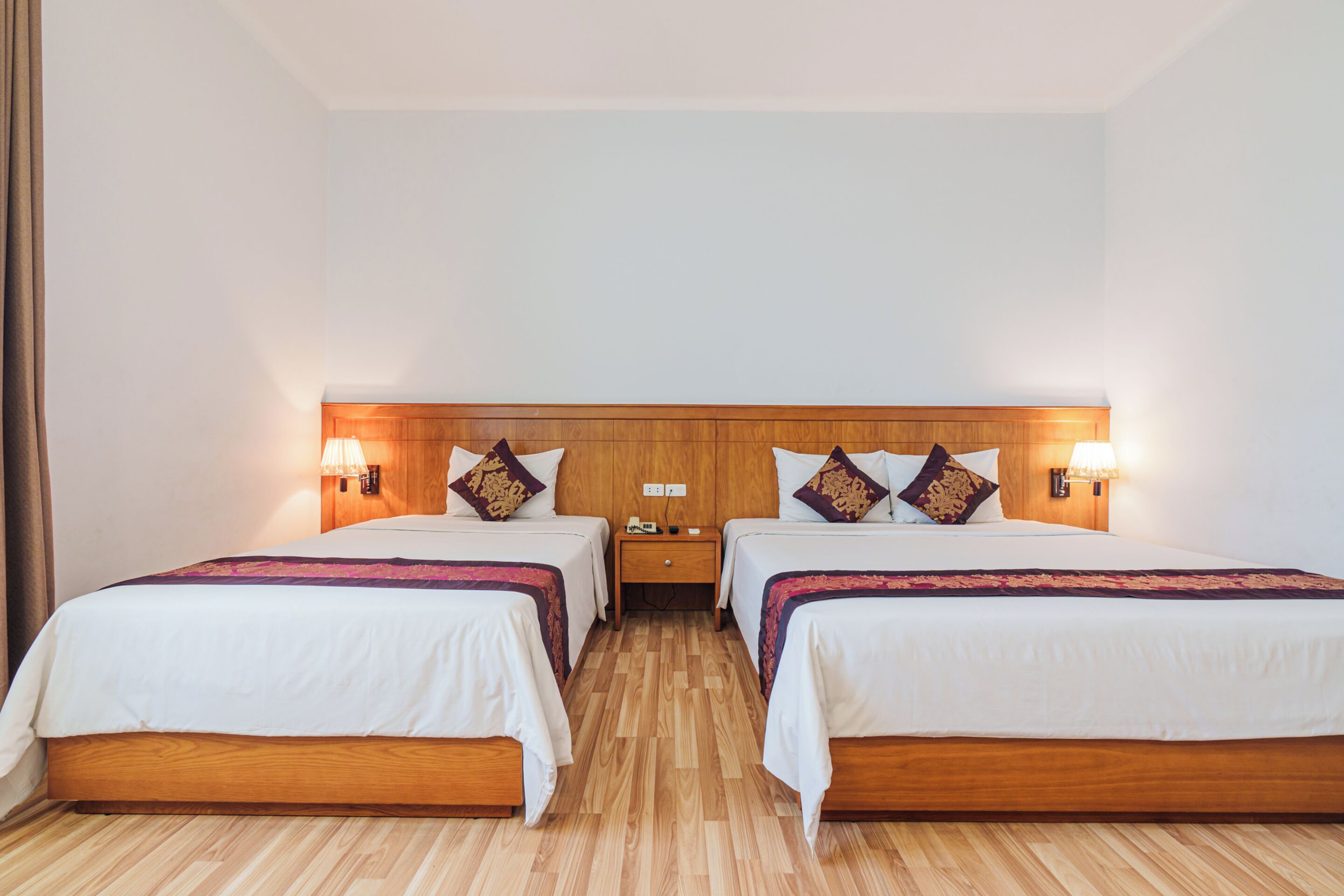 A double room with two beds, wooden headboard, bedside lamps, and a nightstand between the beds.