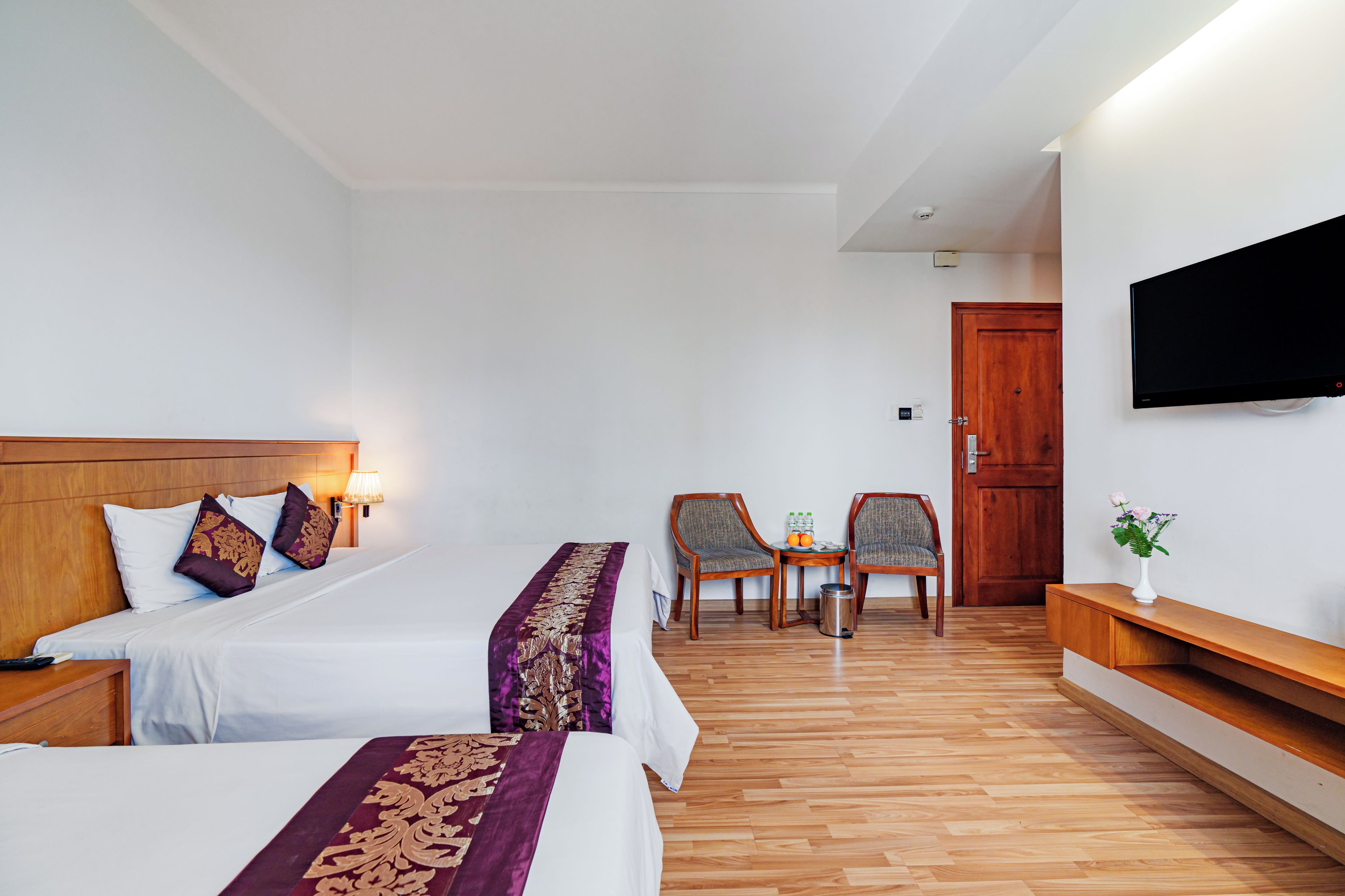 A hotel room with two beds, a TV, a wooden floor, and a small table with chairs.