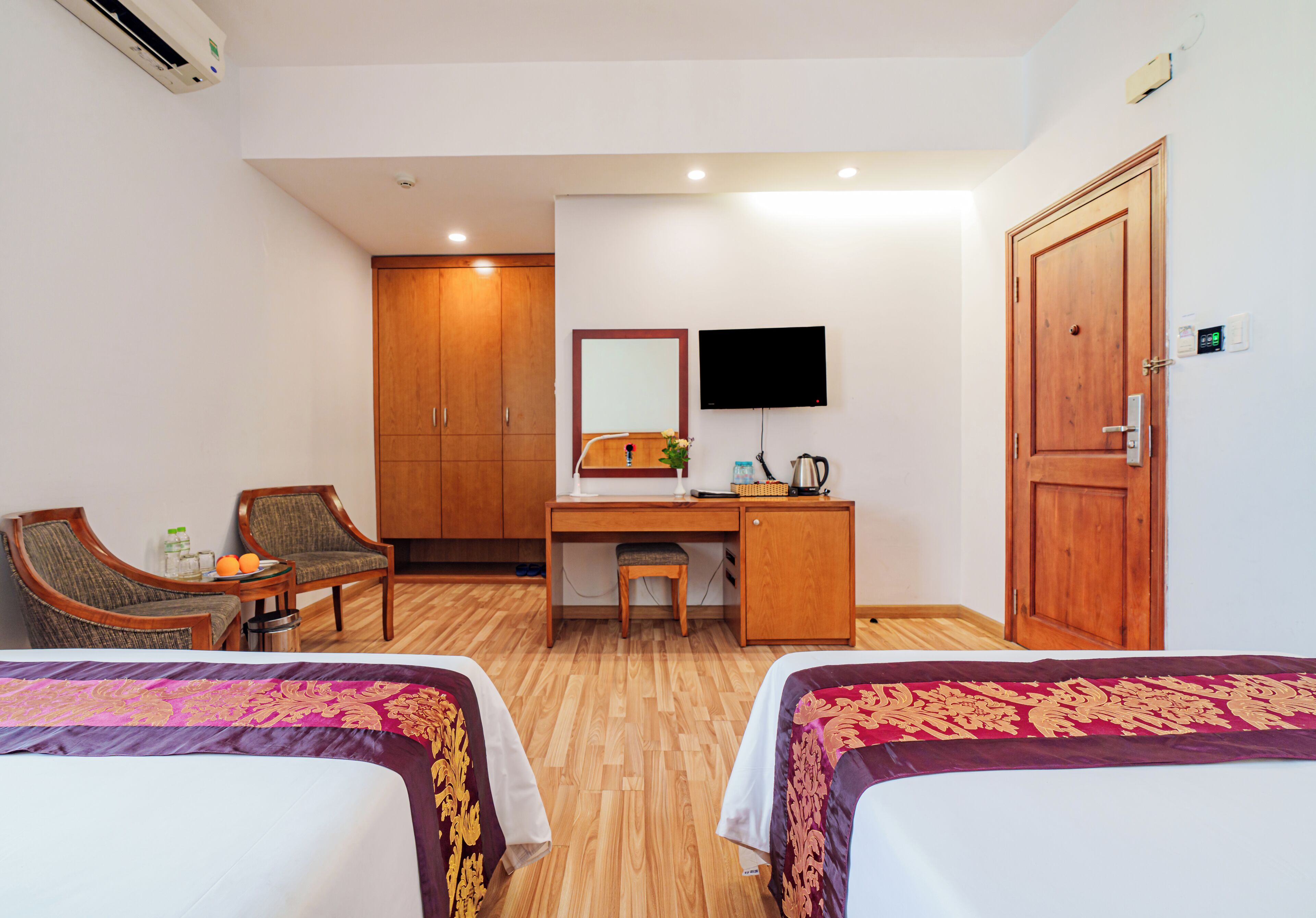 Una habitación de hotel con dos camas, un escritorio con una silla, un televisor y un armario.