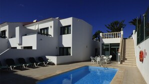 A modern building with a swimming pool, outdoor seating, and a staircase leading to a balcony.